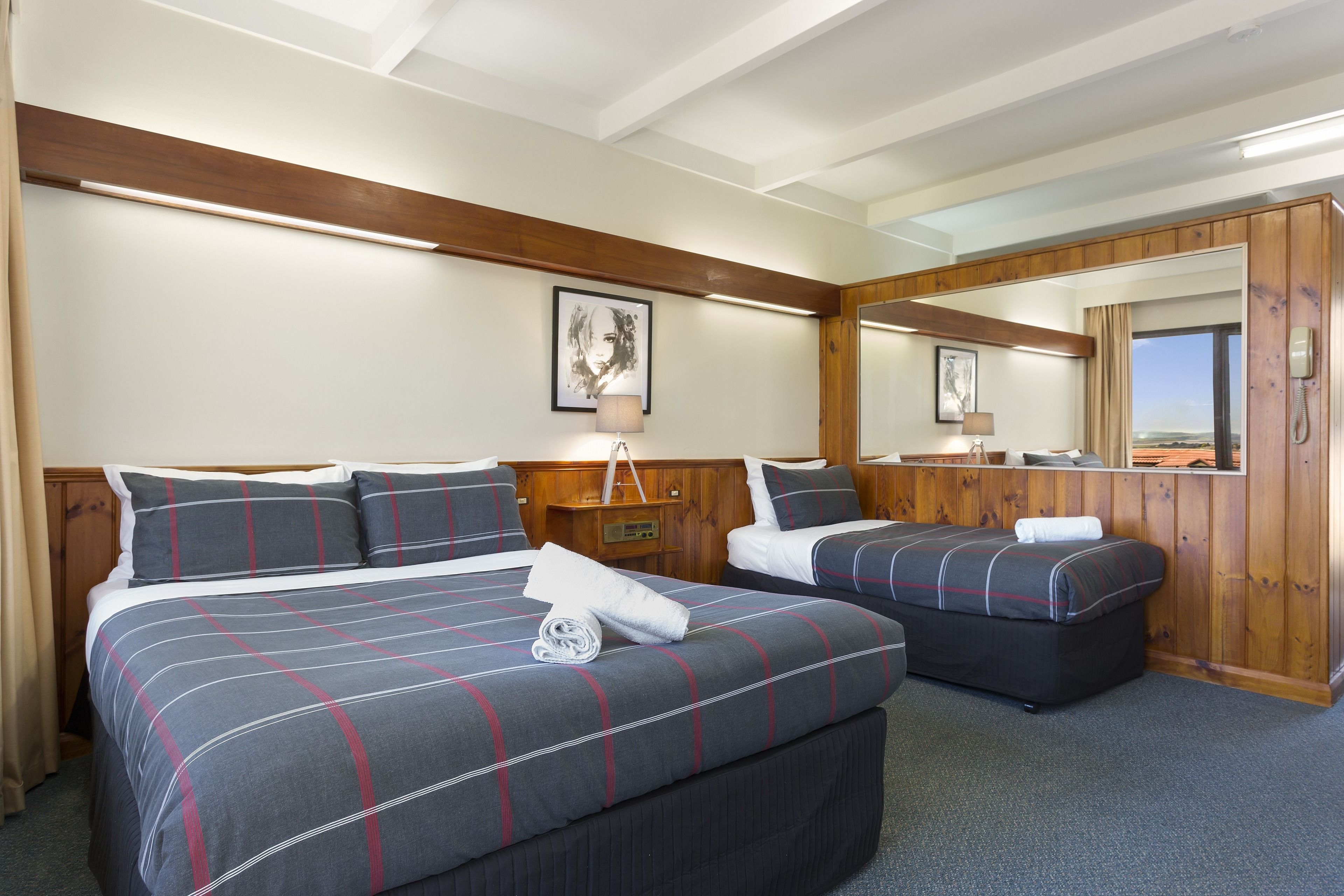 Quarto de hotel com duas camas, painéis de madeira, um espelho grande e vista para o exterior.