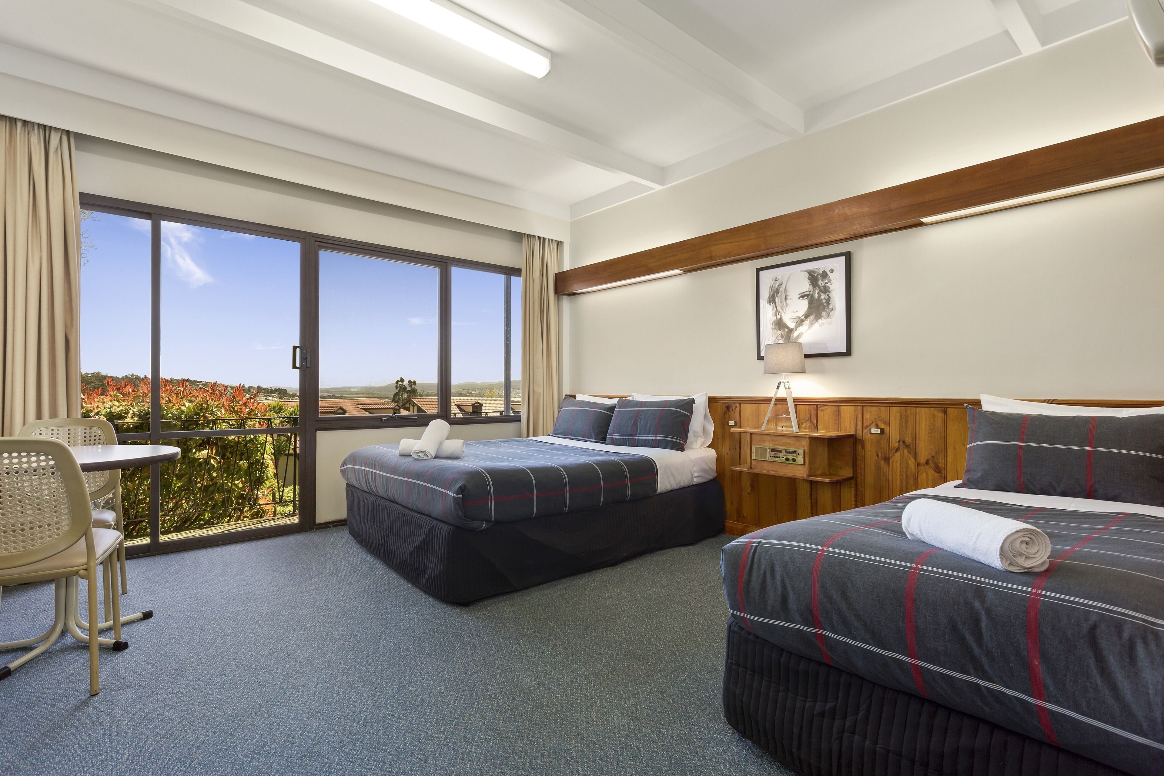 A hotel room with two beds, a desk, and a view of the outdoors.