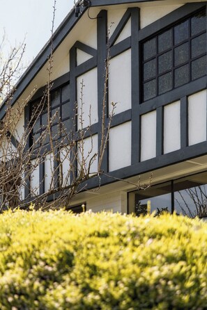 A building with a black and white facade, large windows, and a hedge in the foreground.