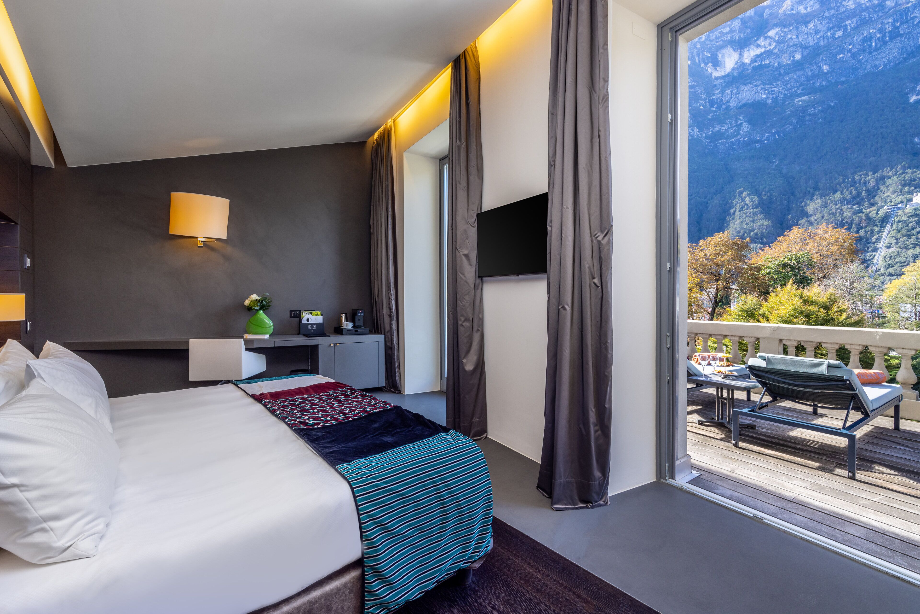 Ein Hotelzimmer mit Bett, Schreibtisch, Fernseher und einem Balkon mit Gartenmöbeln.