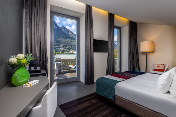 Habitación de hotel con cama, escritorio, un florero con flores, televisor y vistas a montañas.