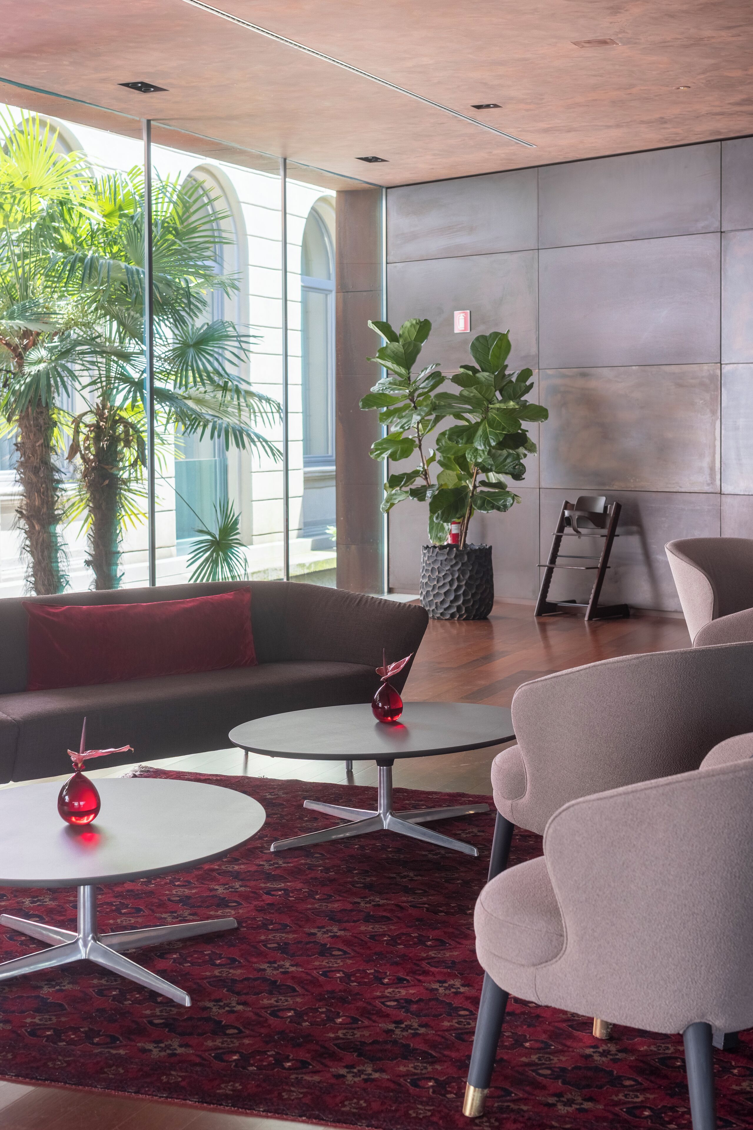 A modern lounge area with a sofa, two round tables, and a large potted plant.
