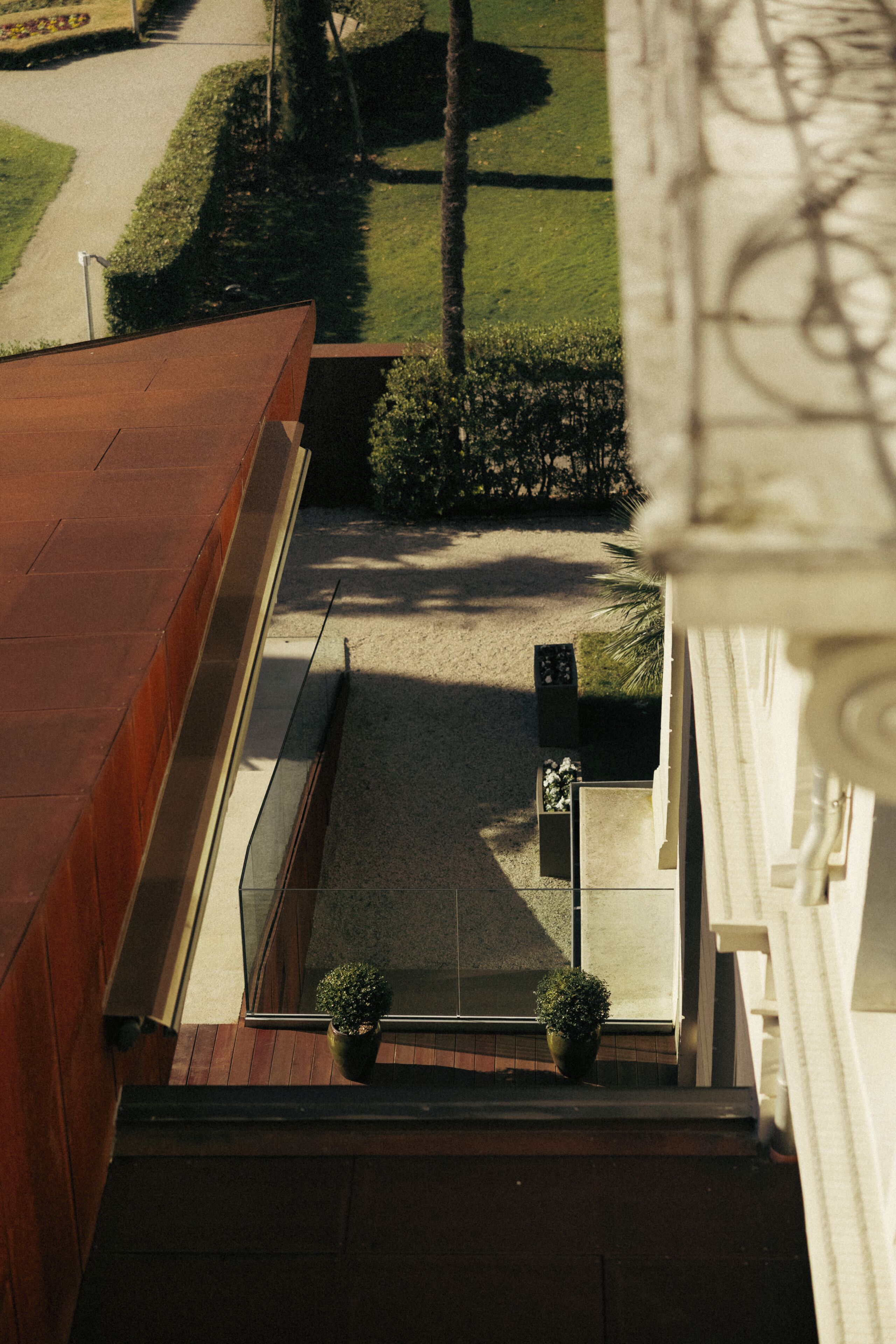An aerial view of a building's exterior with a clear sky, a paved area, and two potted plants on the ground.