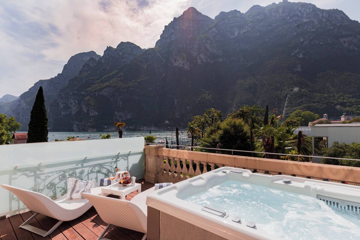 A balcony with a hot tub, wicker chairs, and a view of mountains and a lake.