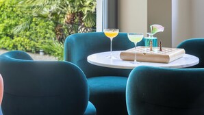 A room with a large window overlooking a mountainous landscape, a table with two drinks and a chessboard, and teal upholstered chairs. - Lido Palace - The Leading Hotels of the World (Riva del Garda)