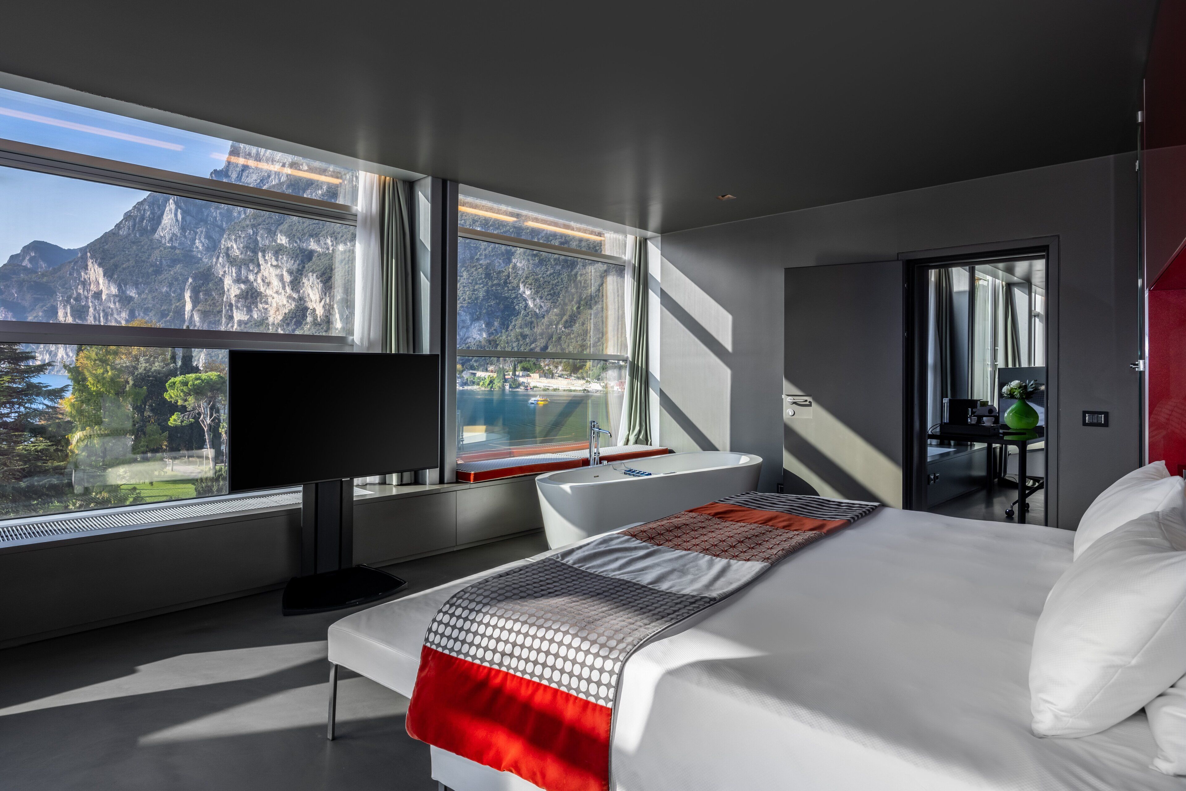 A modern hotel room with a large bed, a TV, a bathtub, and a view of mountains.