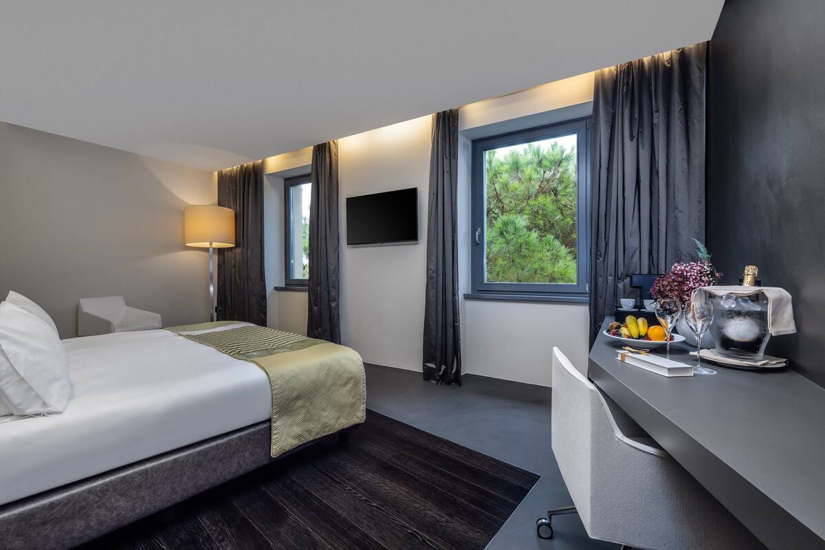 A modern hotel room with a bed, desk, and large windows.