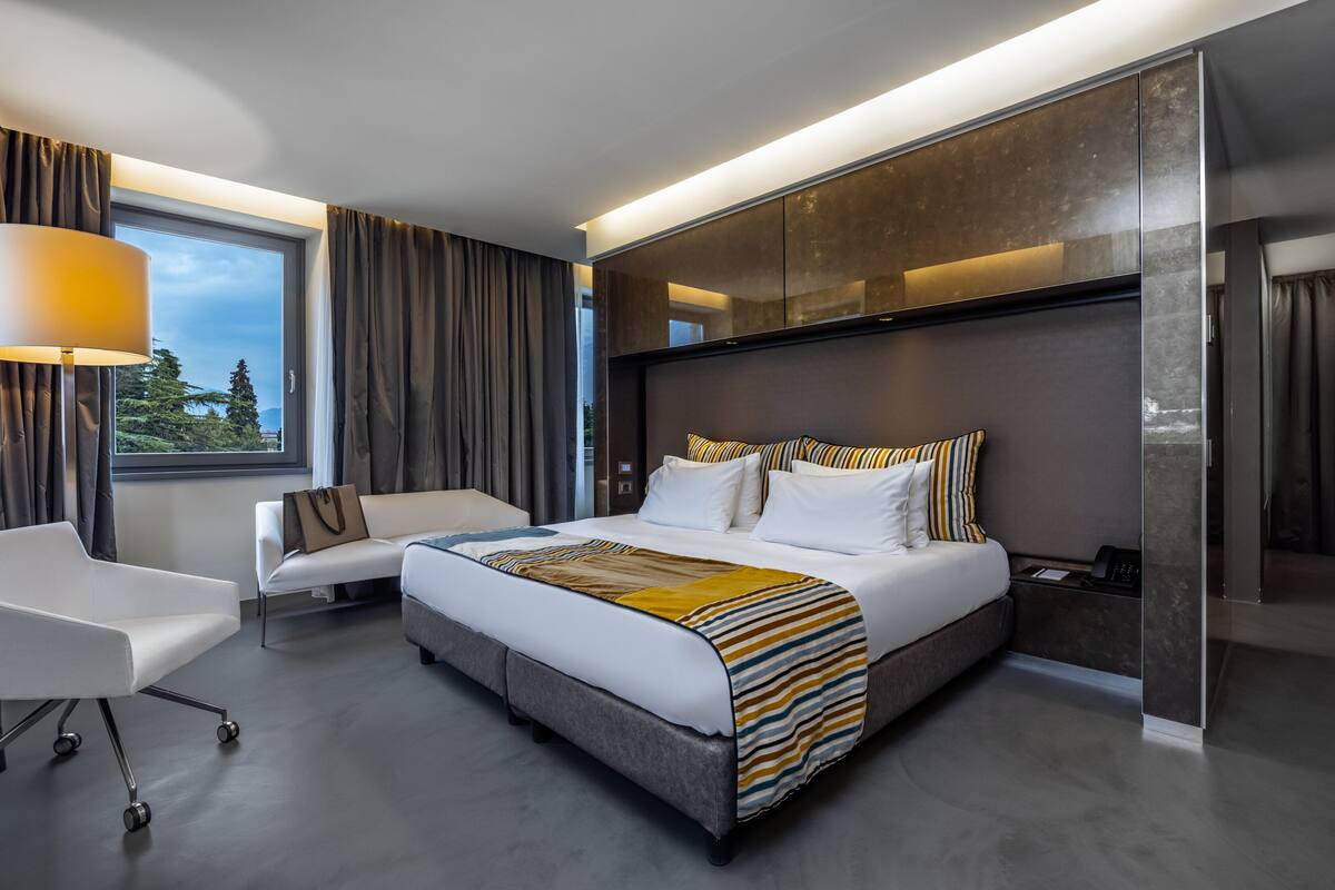 A modern hotel room with a large bed, a sofa, a desk, and a window with curtains.