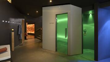A modern spa area with a reception desk, a massage chair, and a glass-enclosed sauna.