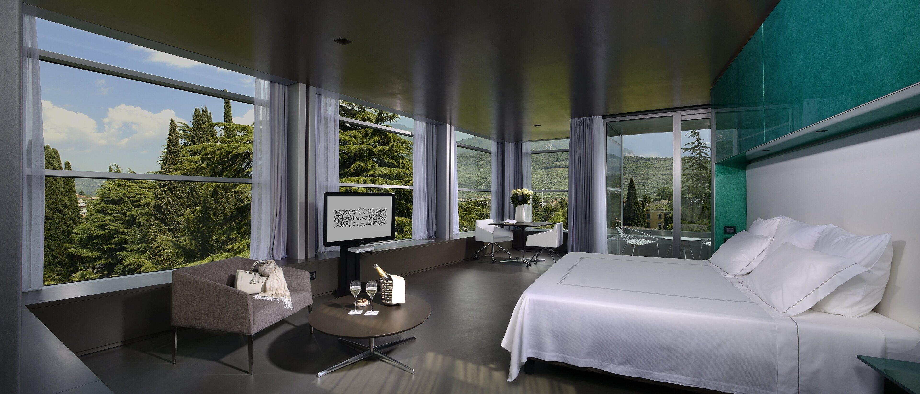 A modern hotel room with a large bed, a desk with a chair, a small sofa, and a view of the outdoors.