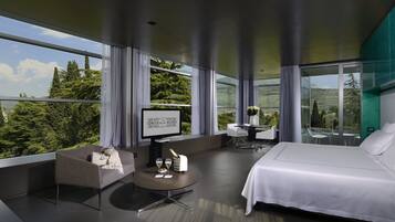 A modern hotel room with a large bed, a desk with a chair, a small sofa, and a view of the outdoors.