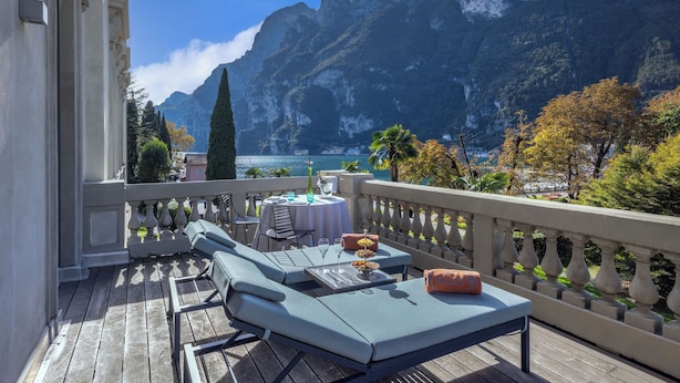 A balcony with a table set for two, overlooking a mountainous coastline. - Lido Palace - The Leading Hotels of the World (Riva del Garda)
