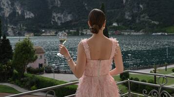 Una mujer con un vestido rosa de pie en un balcón con vista a un lago y montañas.