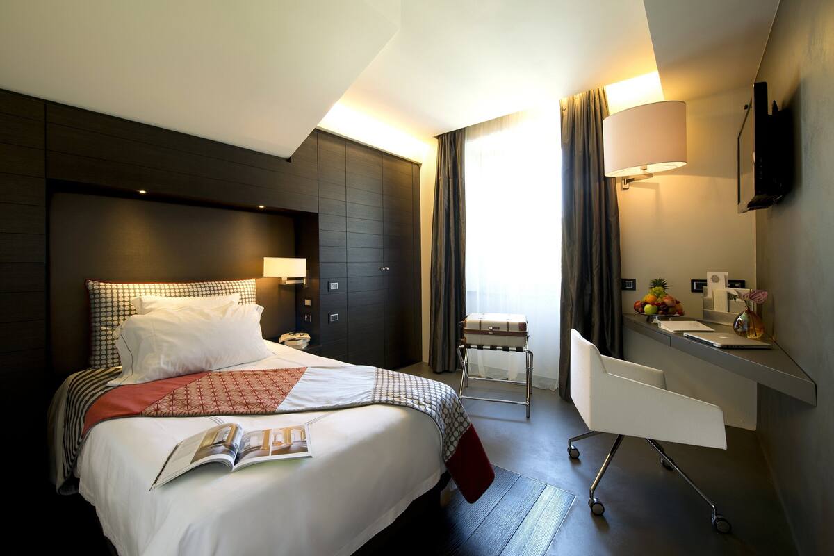 A hotel room with a bed, bedside table, lamp, and a desk with a chair.