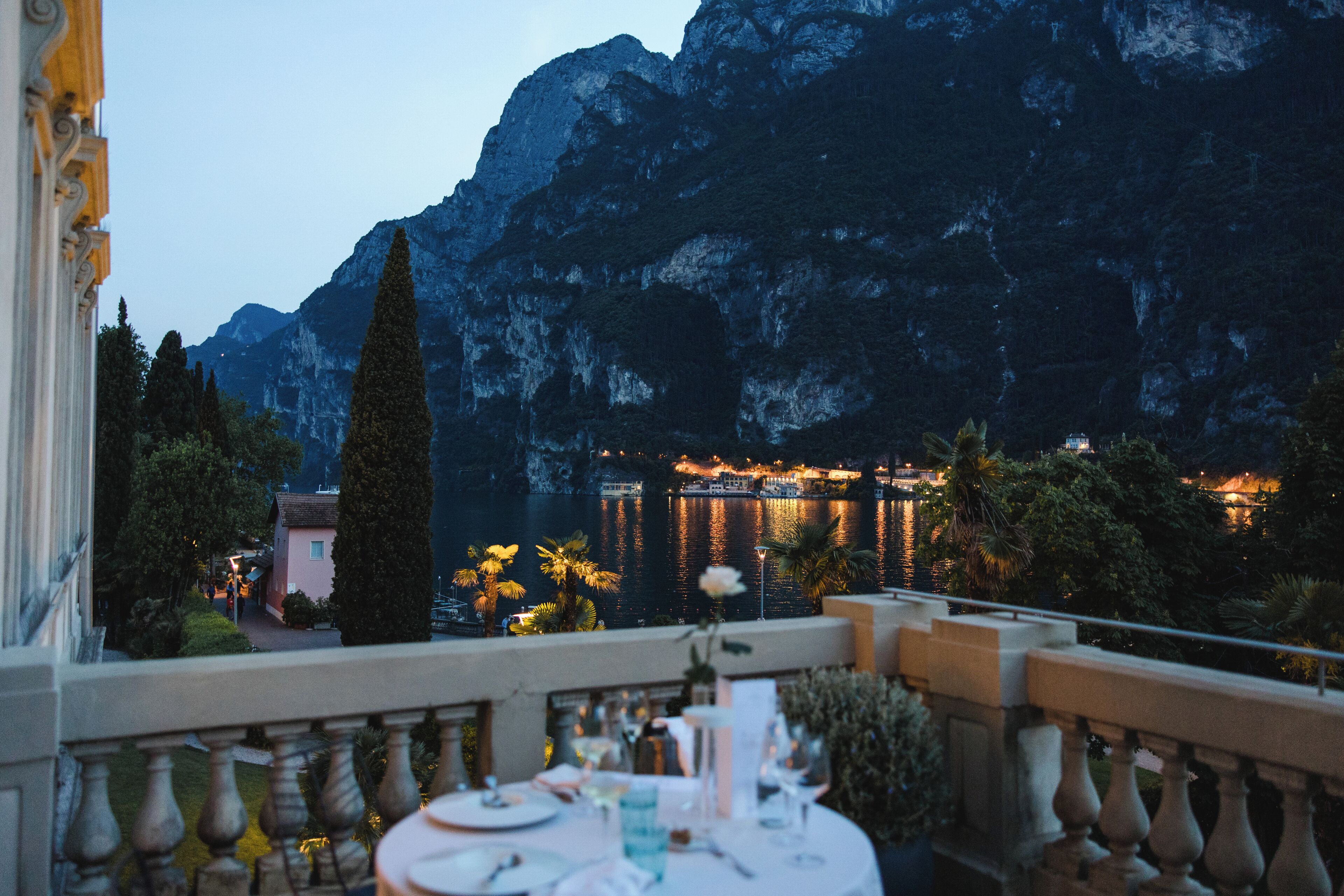 Una terraza con mesa lista para comer, con vista a un paisaje montañoso y un puerto iluminado.