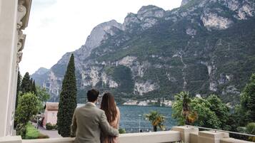 Una pareja en un balcón con vistas a un lago montañoso y un edificio al frente.