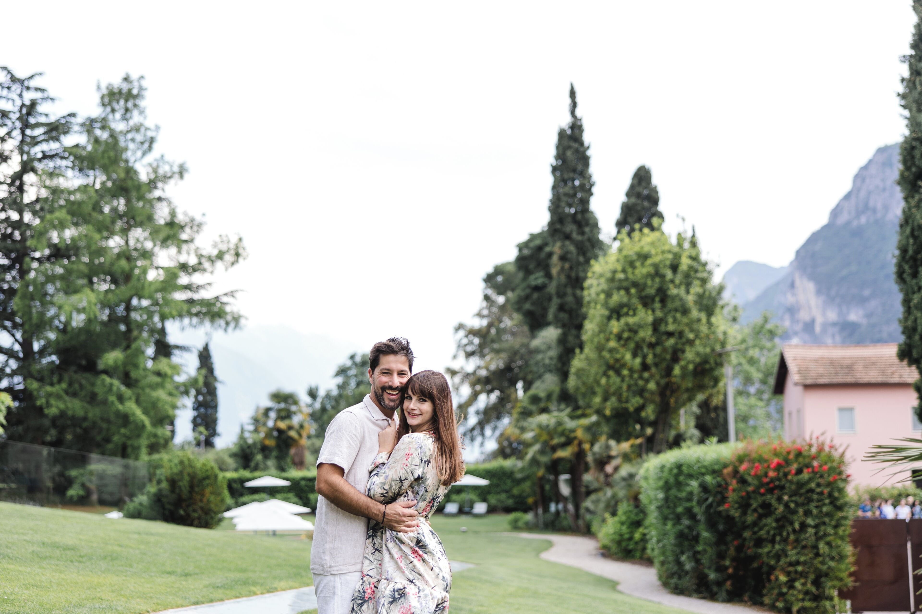 Una pareja abrazándose en un exuberante jardín con montañas al fondo.