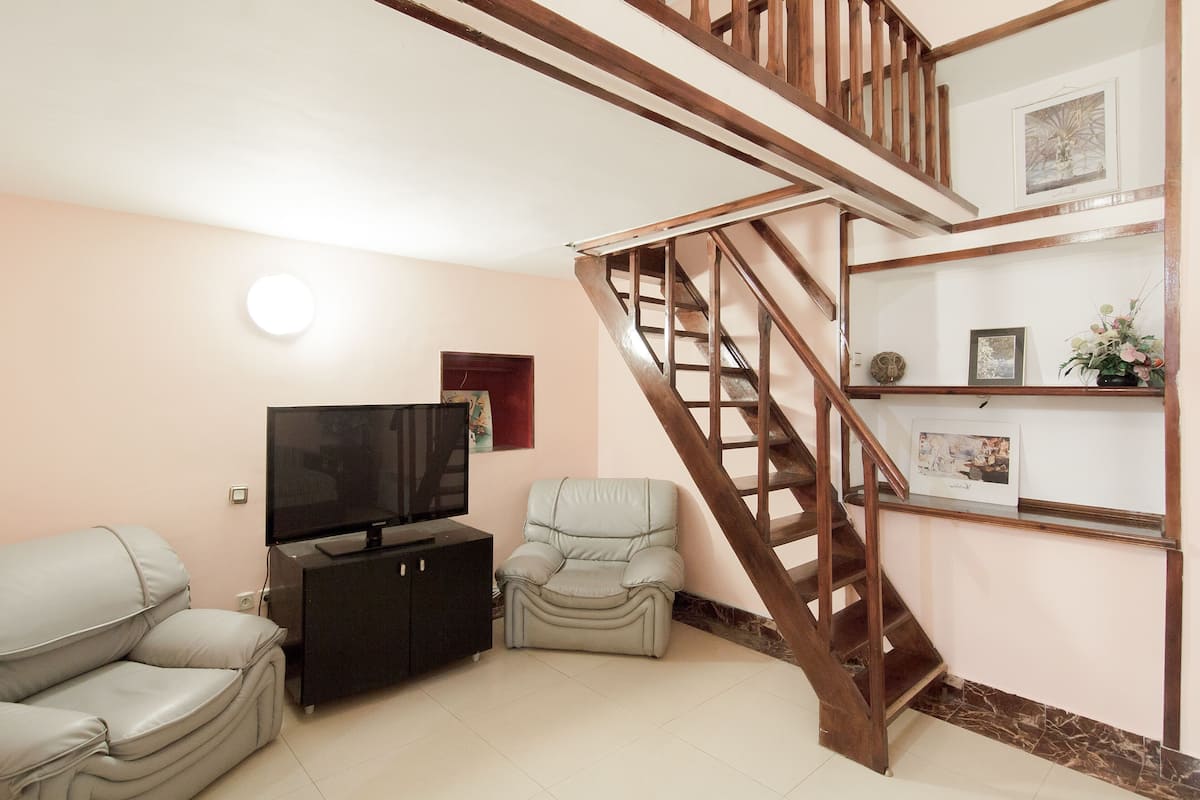 A living room with a sofa, a recliner, a TV, and a staircase.