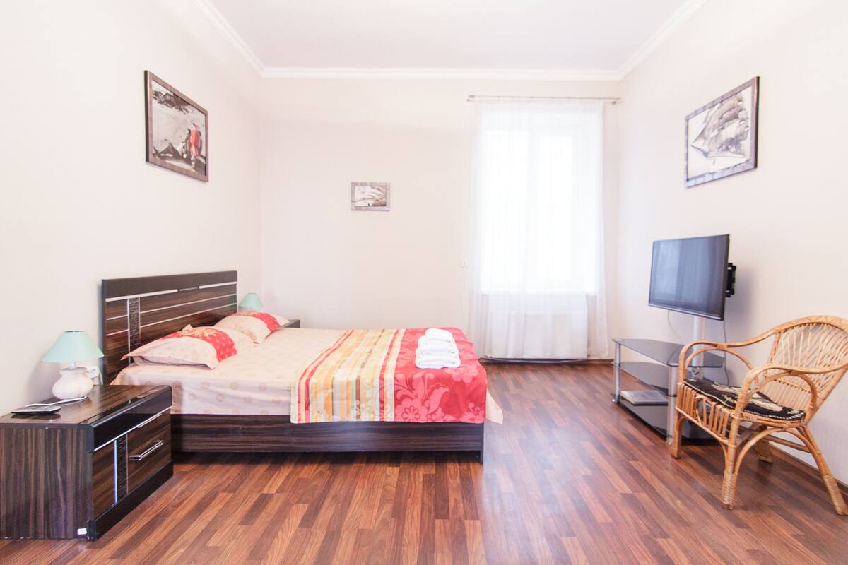 A bedroom with a bed, a TV, a chair, and a desk.