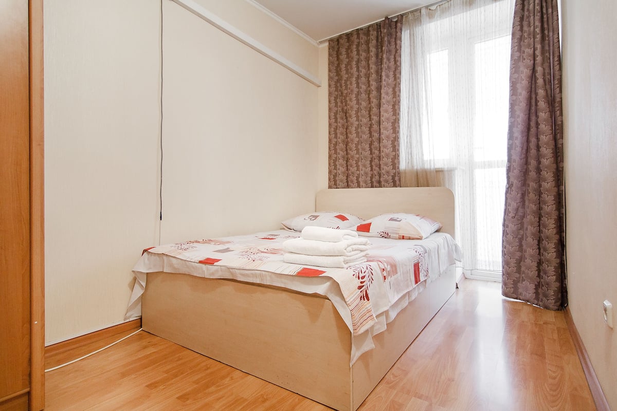 A bedroom with a bed, a window with curtains, and a wooden floor.