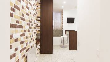 A hallway with a brick-patterned wall, a wooden door, a small round table, and a flat-screen TV mounted on the wall.