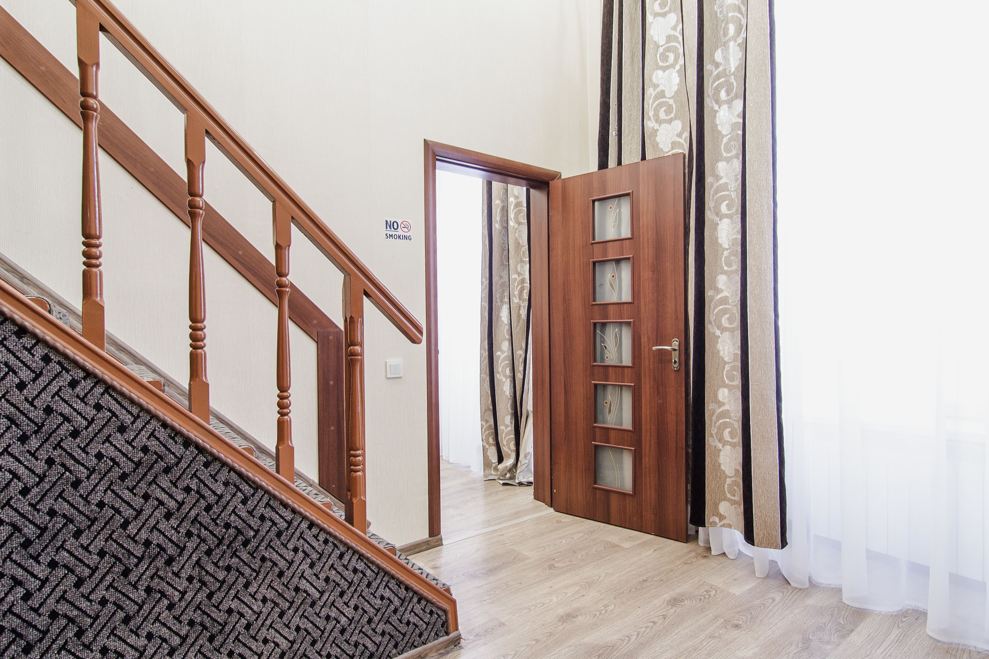 A wooden staircase with a patterned carpet leading to a room with a wooden door and a glass panel.