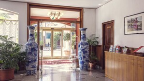 A reception area with a wooden desk, two large vases, and a door leading to a lobby. - Hotel Tre Laghi (Nebbiuno)