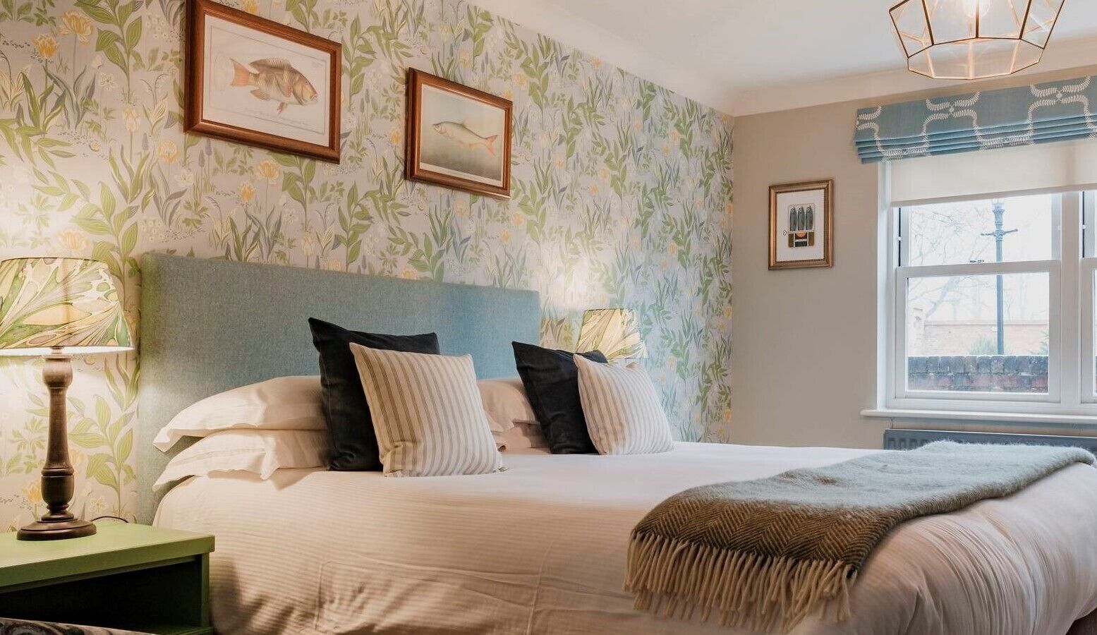 A bedroom with a bed, pillows, a nightstand, a lamp, and framed pictures on the wall.