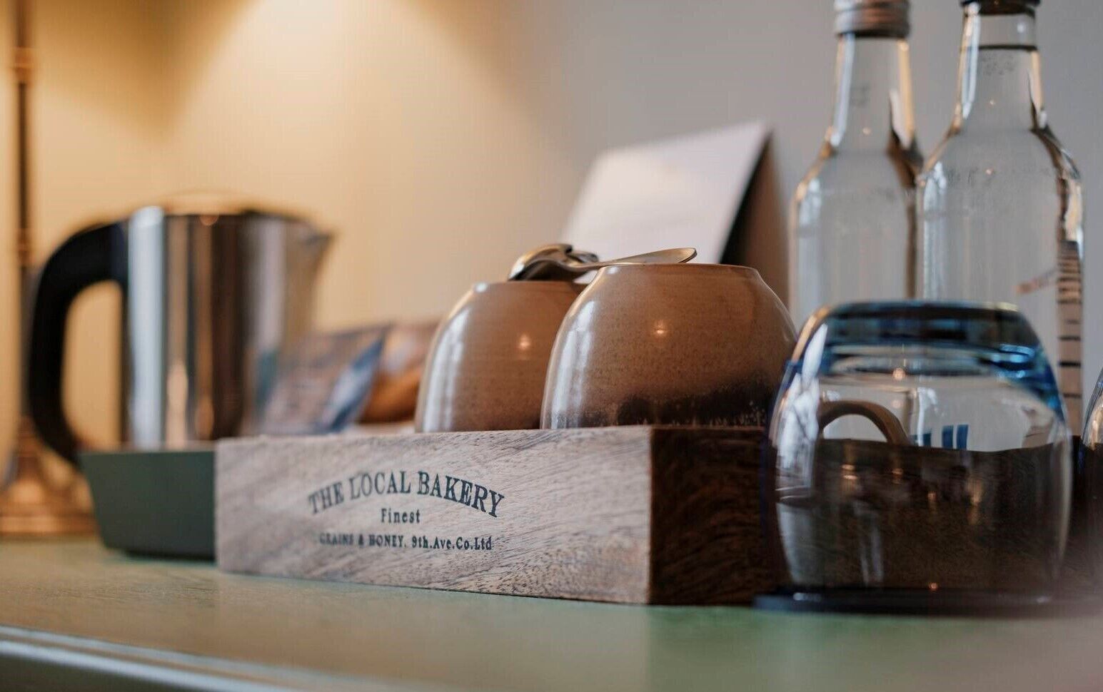 Une boîte en bois portant l’inscription « La boulangerie du coin », avec du pain et une théière posés sur une table.