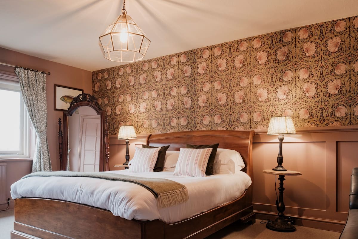 Un lit bien fait, avec une tête de lit en bois, deux lampes de chevet et un papier peint à motifs.