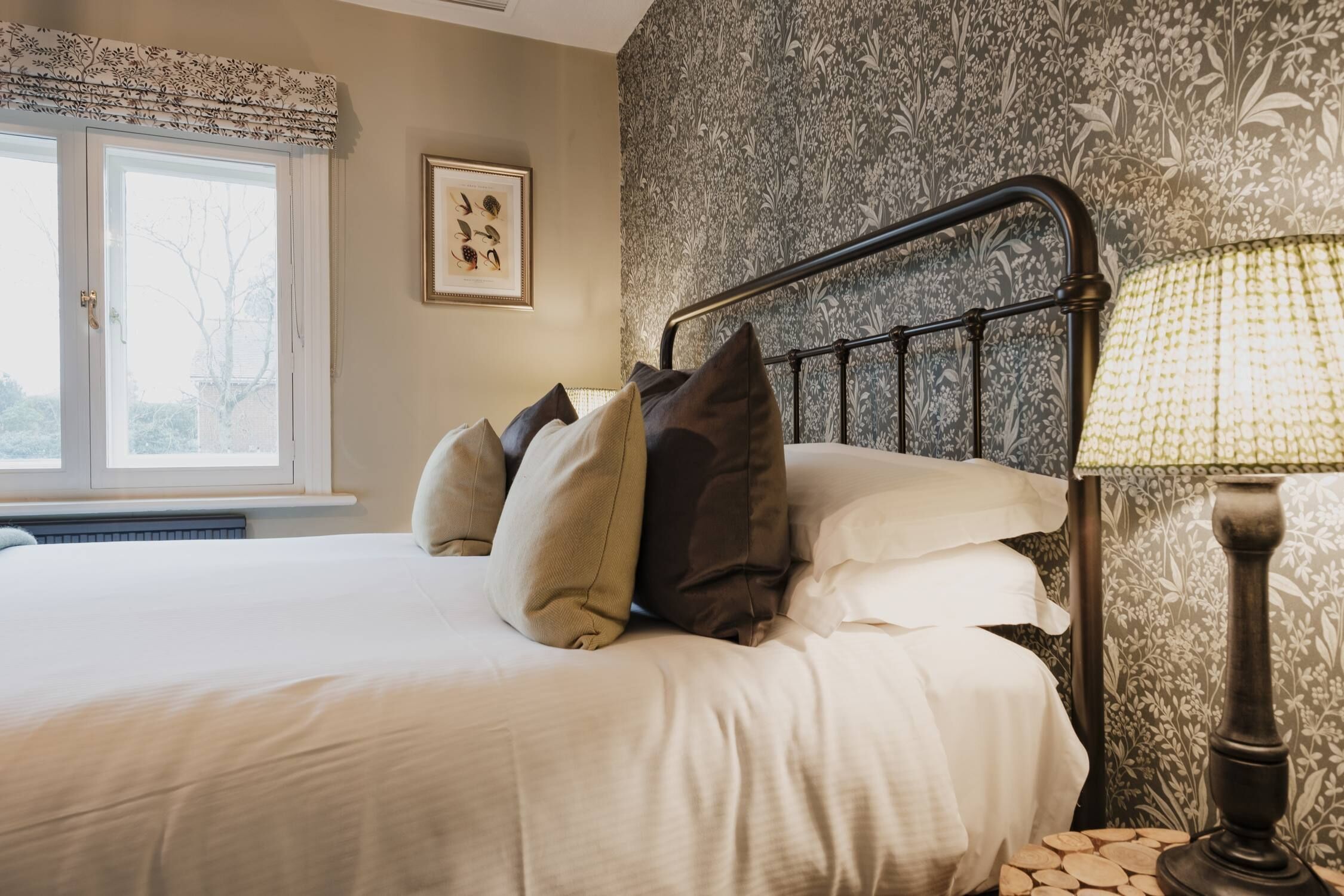 A neatly made bed with pillows, a bedside lamp, and a framed picture on the wall.