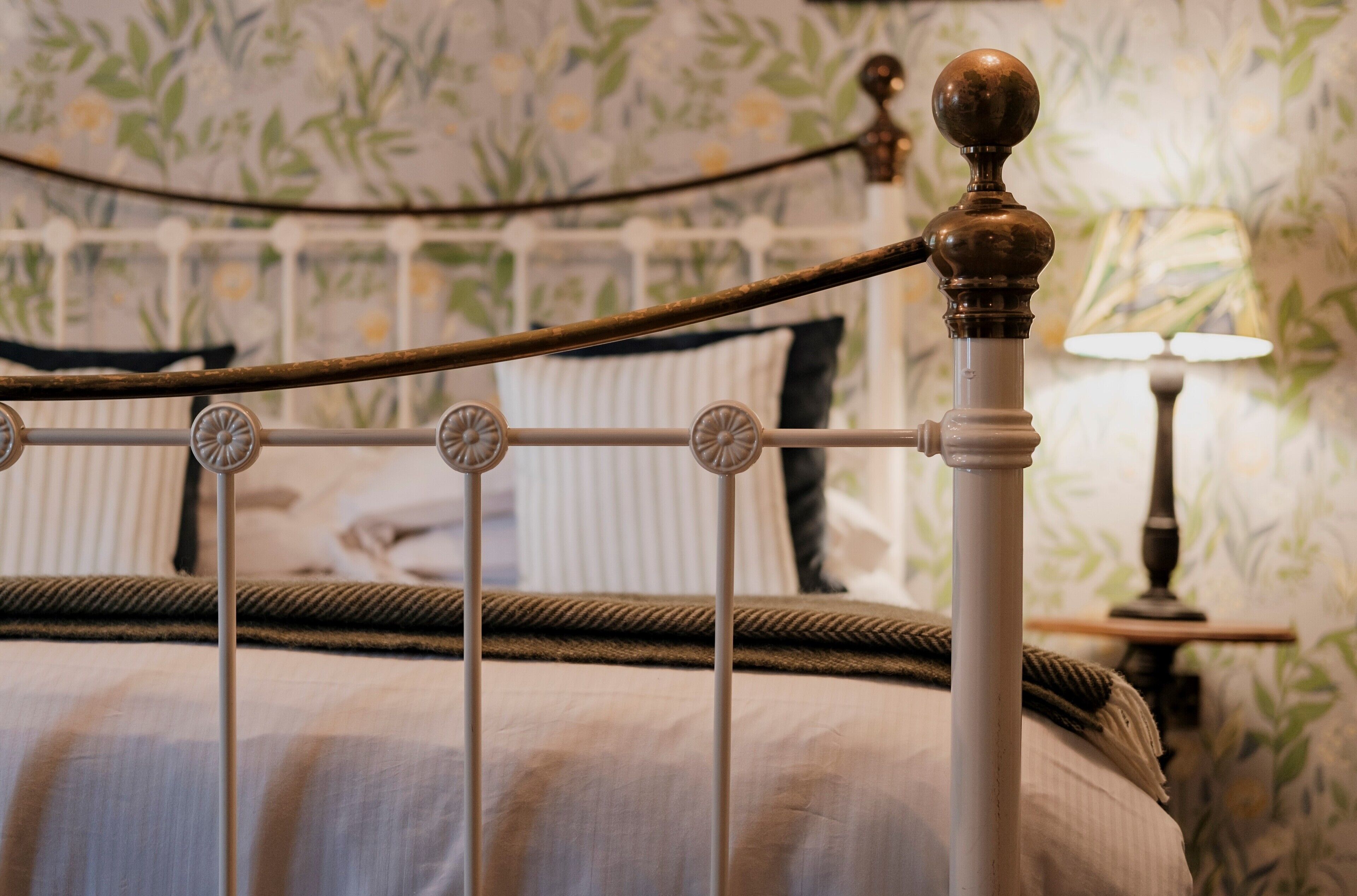 A bed with a metal headboard, a decorative lamp, and a floral wallpaper pattern.