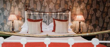 A bed with white metal headboard and footboard, two red pillows, and two lamps on either side.
