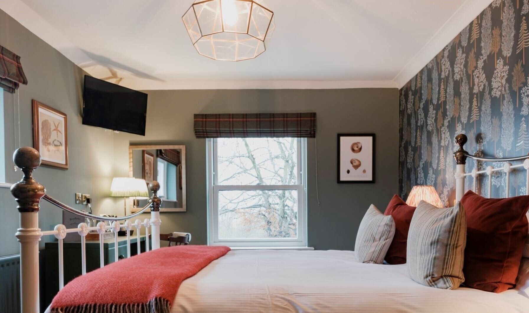 A bedroom with a large bed, a window with a view of trees, a mirror, and a television on the wall.