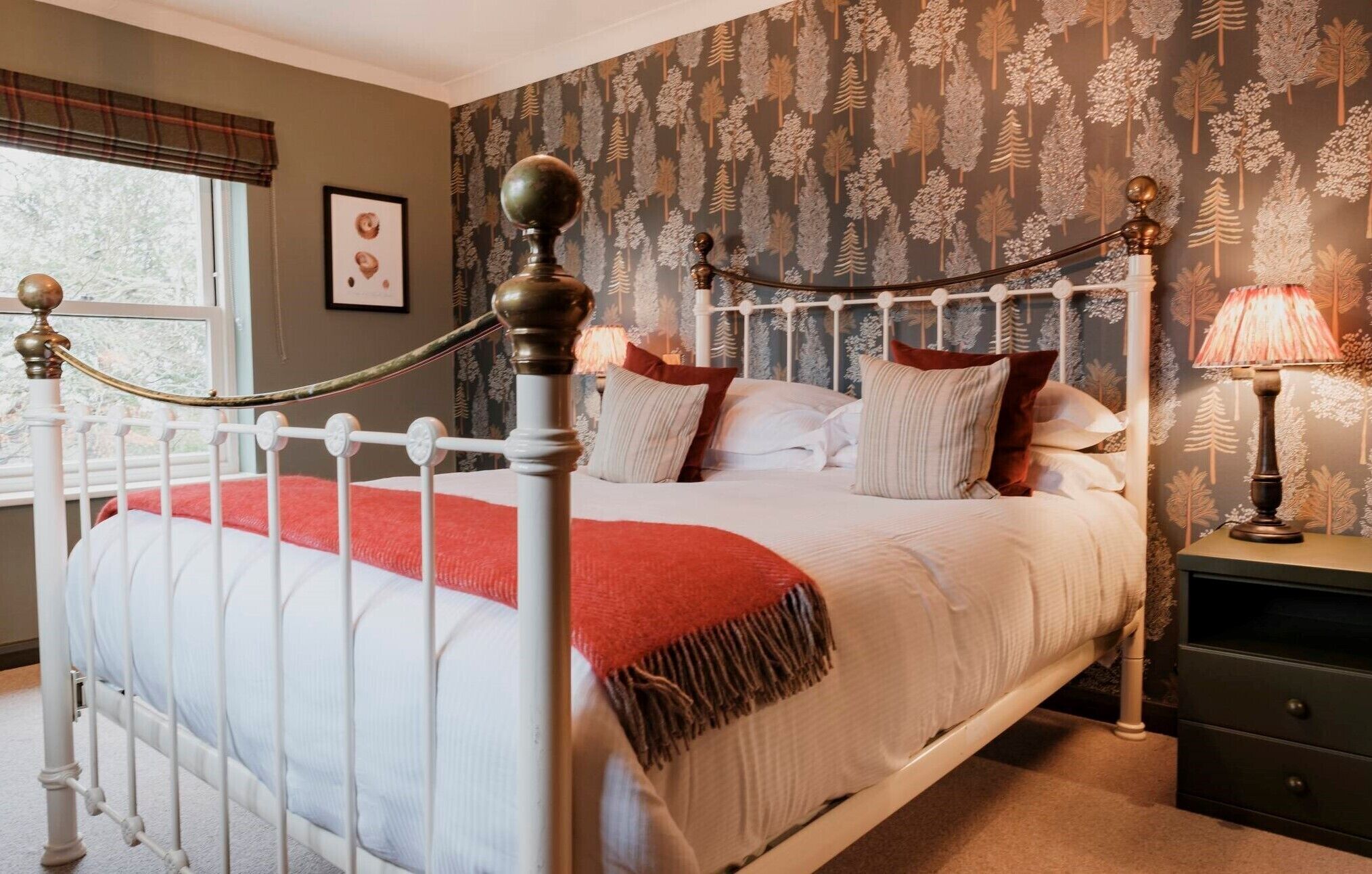 A neatly made bed with a white and red bedspread, a wooden headboard, and a bedside table with a lamp.