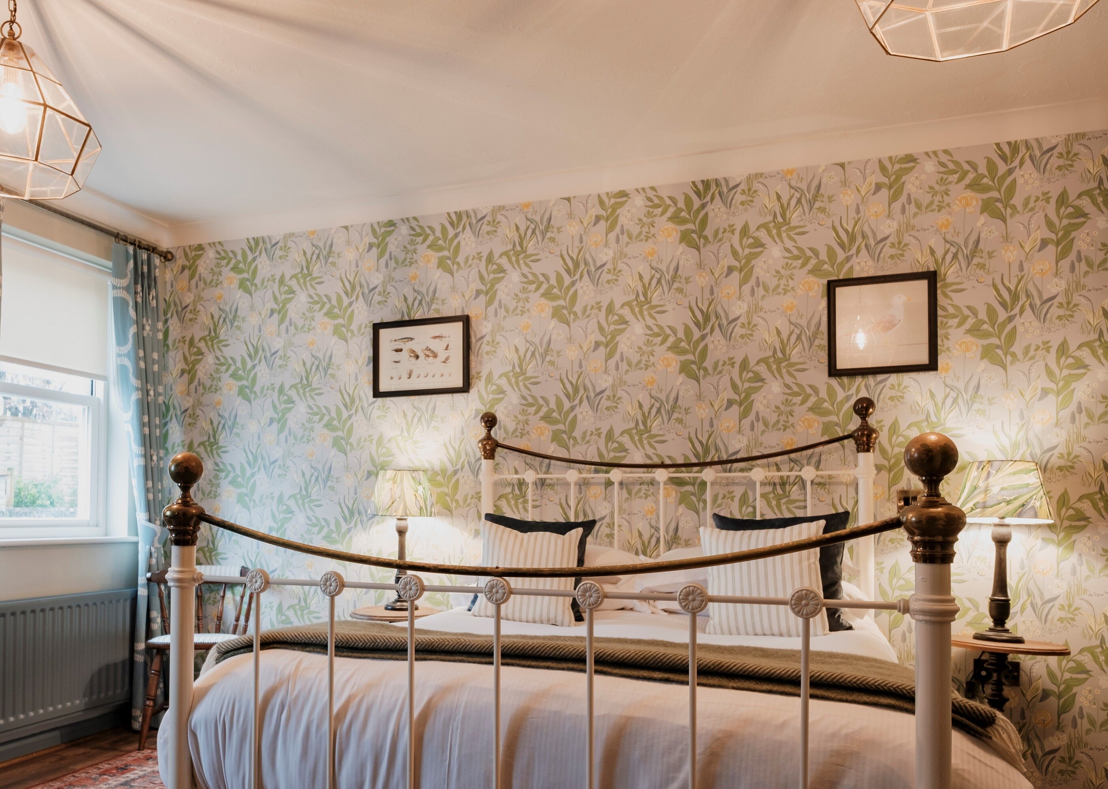 Un dormitorio con cama con dosel, papel tapiz floral y una ventana con cortinas.