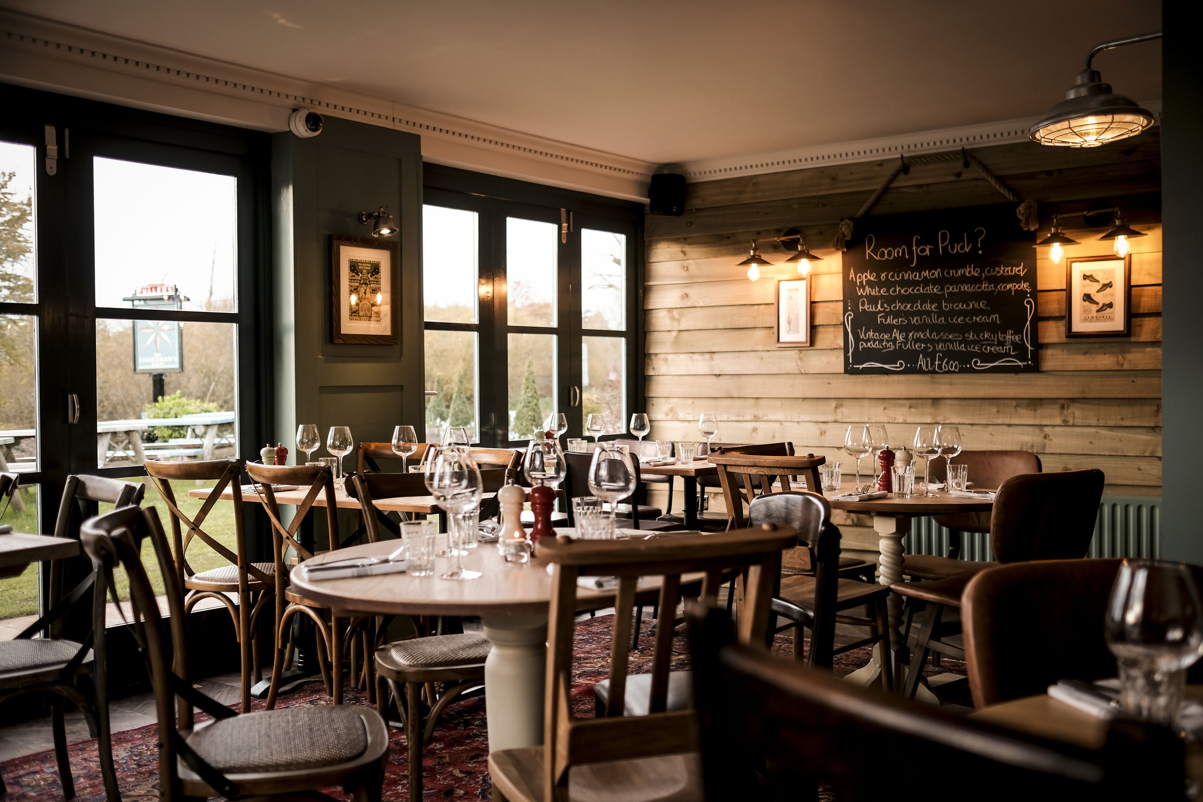 A restaurant with wooden walls, multiple tables, and chairs, and a chalkboard menu on the wall.