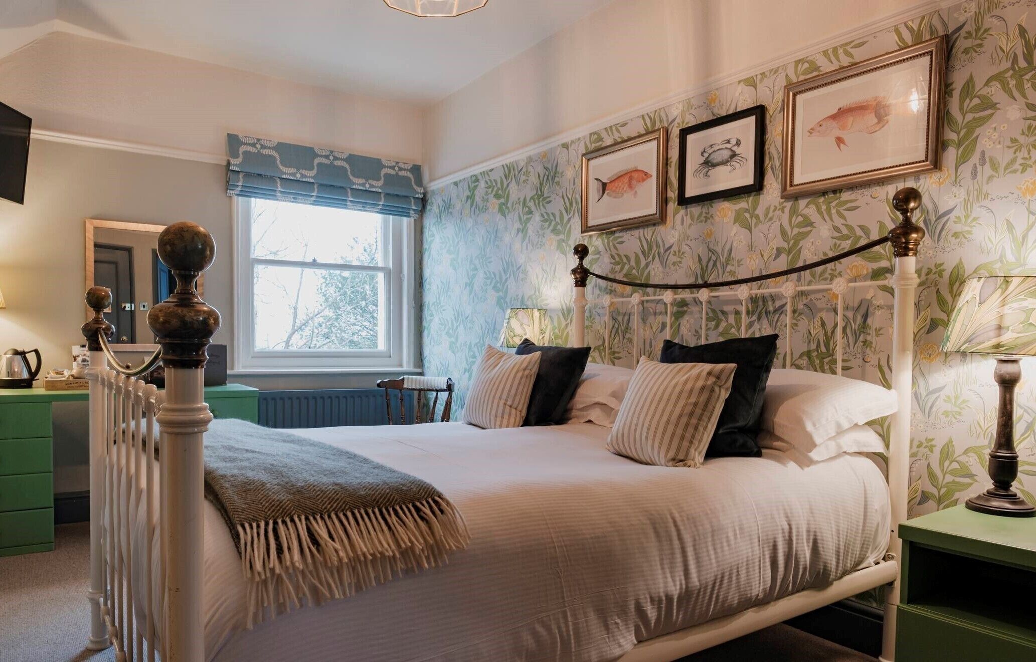A bedroom with a bed, a radiator, a window, and floral wallpaper.