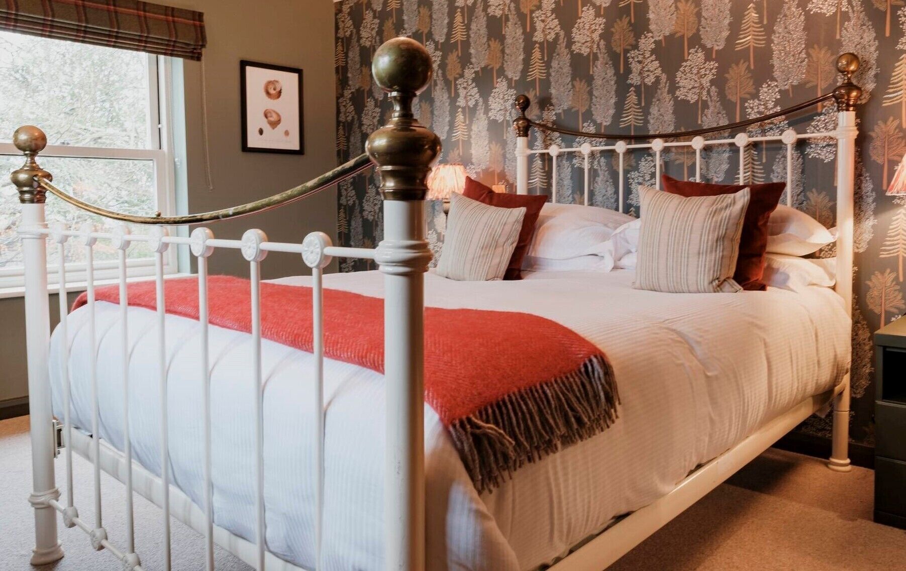 A bed with a white metal frame, a red throw blanket, and multiple pillows.