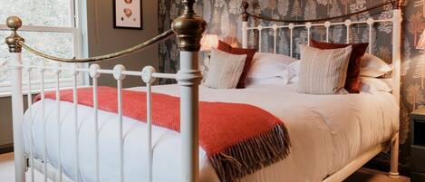 A bed with a white metal frame, a red throw blanket, and multiple pillows.