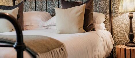A neatly made bed with white linens and multiple pillows, a metal headboard, and a wooden nightstand with a lamp.