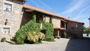 A stone building with a red-tiled roof, ivy-covered walls, and a cobblestone courtyard. - Casa do Redondo (Meda)