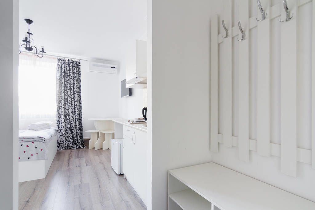 A modern, white-themed bedroom with a bed, bedside table, and a window with patterned curtains.