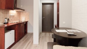 A compact kitchen with wooden cabinets, a built-in oven, and a small refrigerator. There's a dining table with a remote control on it. - Odessa Rent Service Apartments at Sea-side (Odesa)