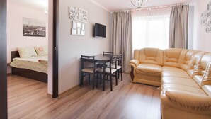 A living room with a sofa, a dining table with chairs, a flat-screen TV, and a bed with a polka dot bedspread. - Odessa Rent Service Apartments at Sea-side (Odesa)