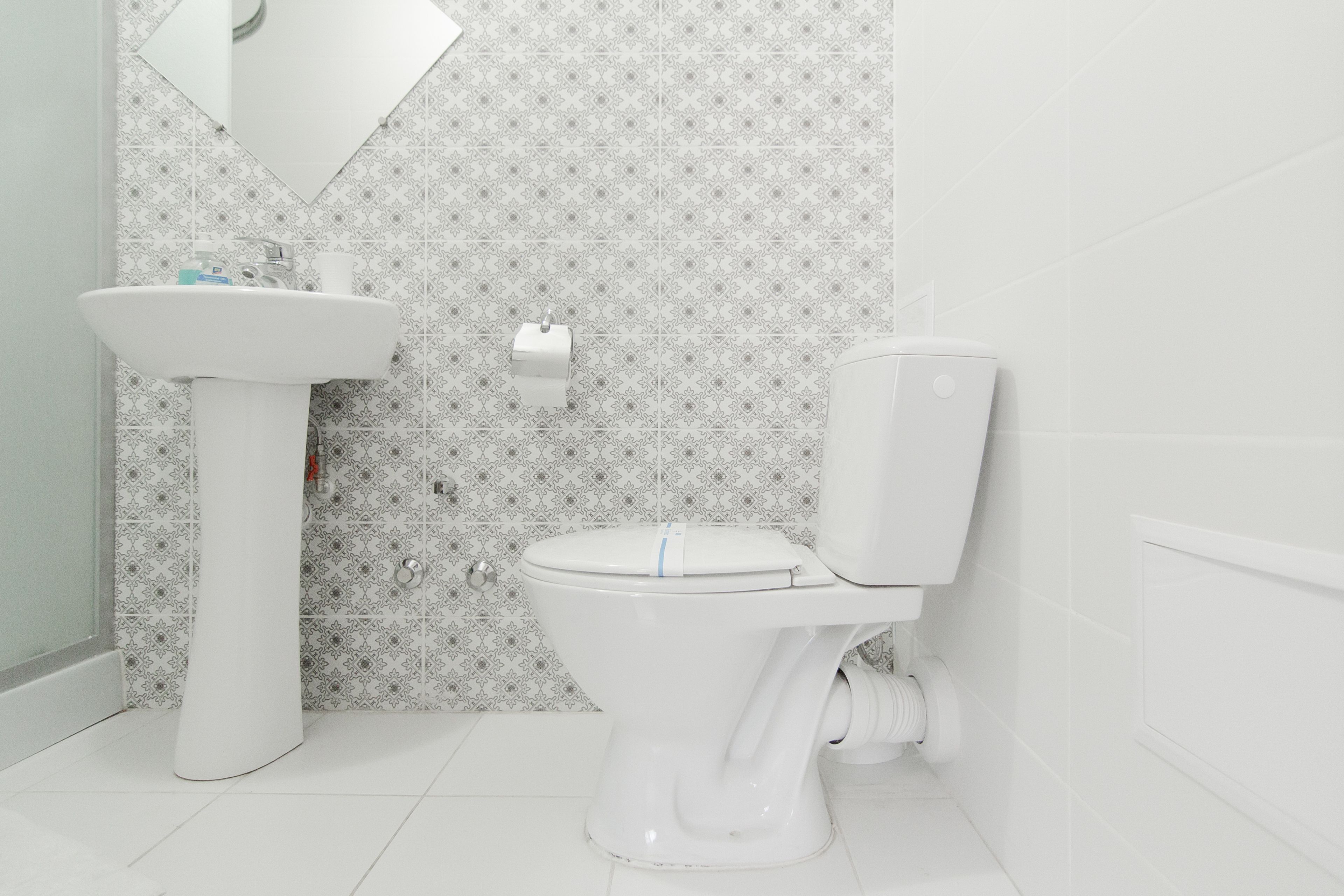 Casa de banho com lavatório branco, sanita e azulejos estampados.