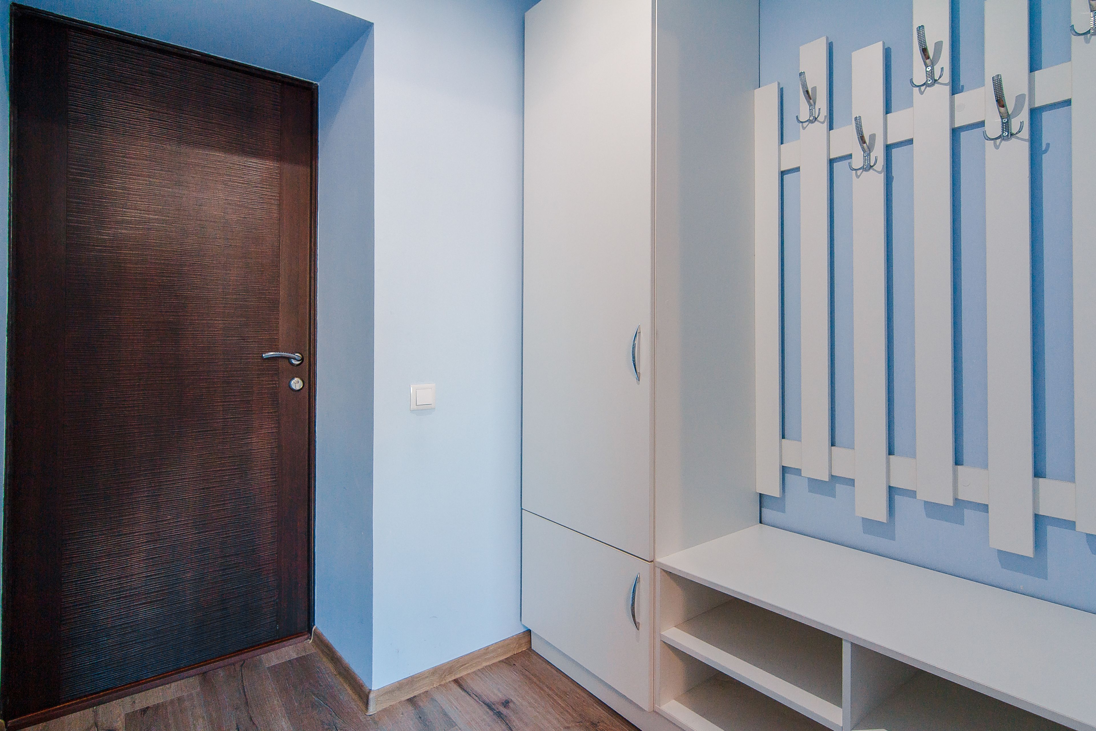A room with a wooden door, a white wardrobe, and a white shelf unit with hooks.