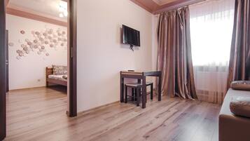 Une chambre avec un lit, un bureau, une télévision et une fenêtre avec des rideaux.
