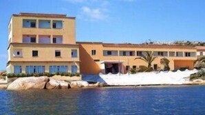 A multi-story hotel with a pool, featuring a flat roof and a large rock formation in the foreground. - Hotel Il Gabbiano (La Maddalena)