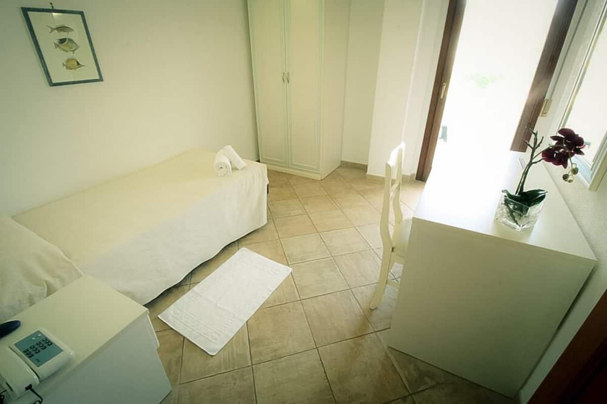 Een nette, kleine kamer met een bed, een bureau met een computer, een kledingkast en een raam met een plant.